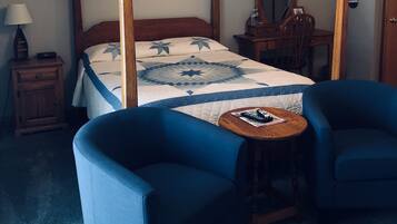 Un letto a baldacchino con copripiumino, due poltrone blu, un tavolino con un telecomando, un comodino con una lampada, uno specchio e una porta con una mazza da baseball appesa.