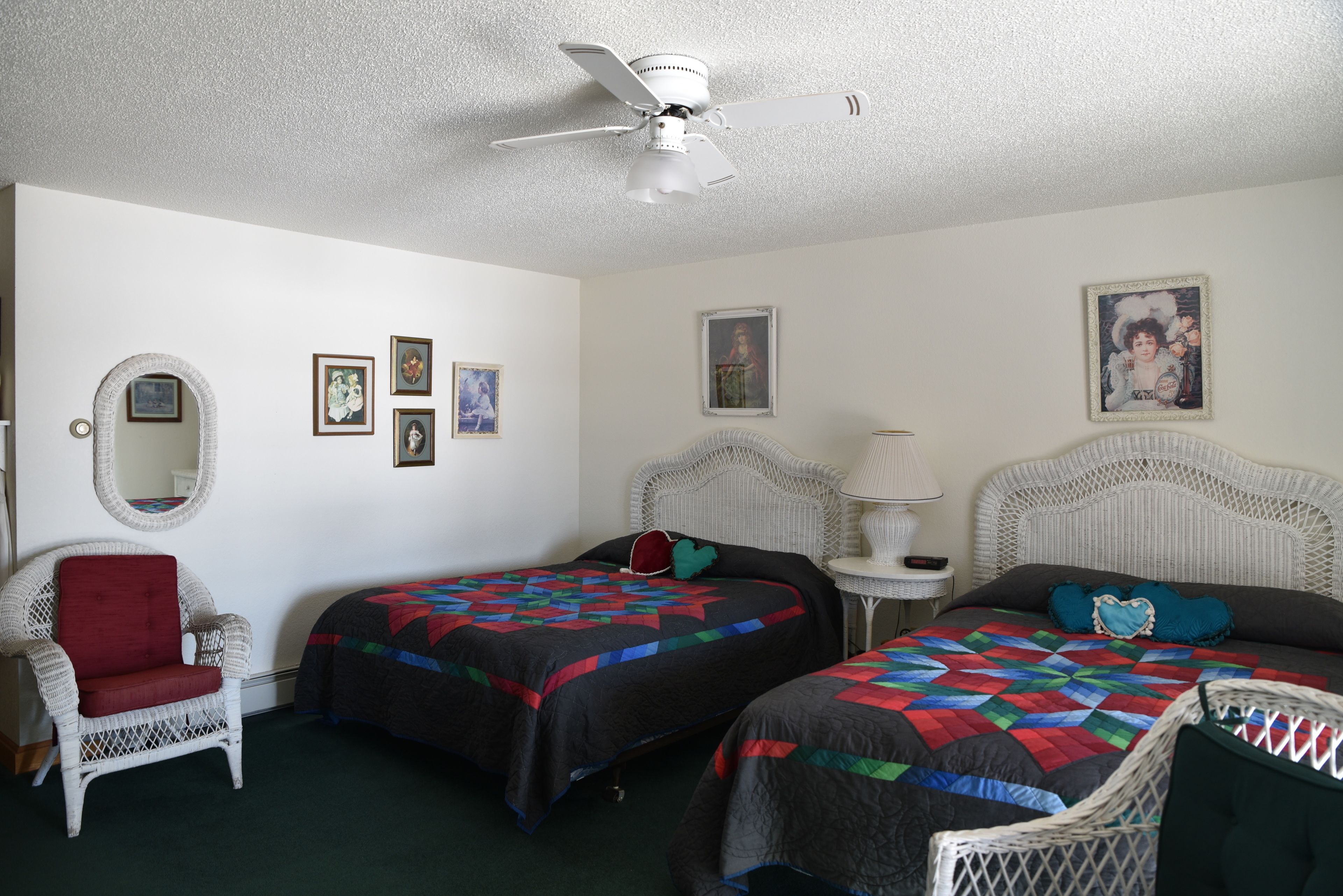 A room with two beds, a chair, a ceiling fan, and framed pictures on the walls.