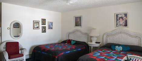 A room with two beds, a chair, a ceiling fan, and framed pictures on the walls.