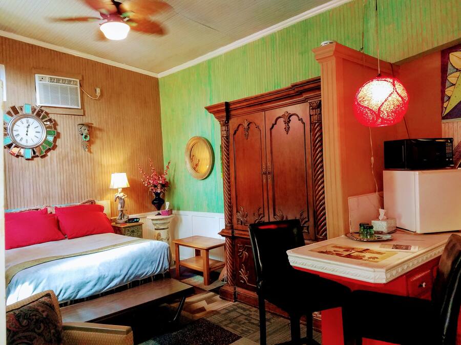 Una habitación con cama, escritorio, silla, reloj, espejo y microondas.