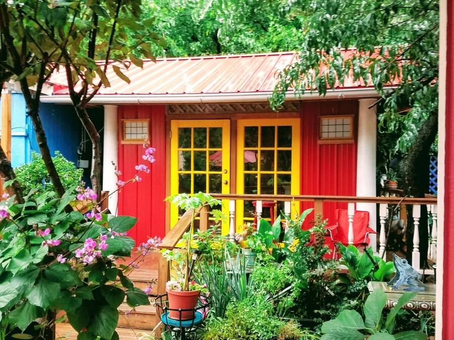 Uma casa colorida com fachada vermelha e amarela, rodeada por vegetação exuberante e plantas em vasos.