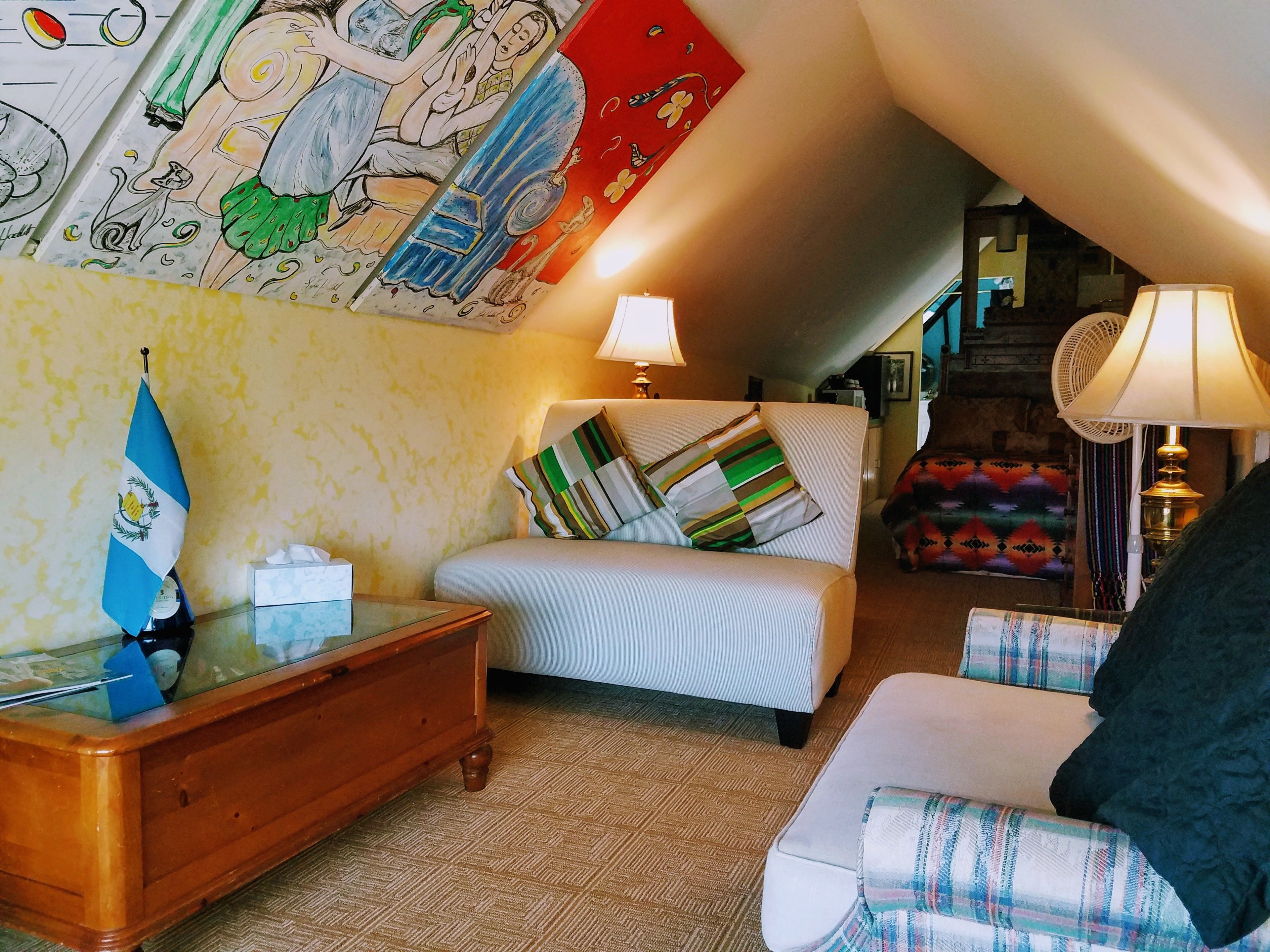 Una habitación acogedora con una cama, una mesita de madera, una bandera y un mural colorido en la pared.
