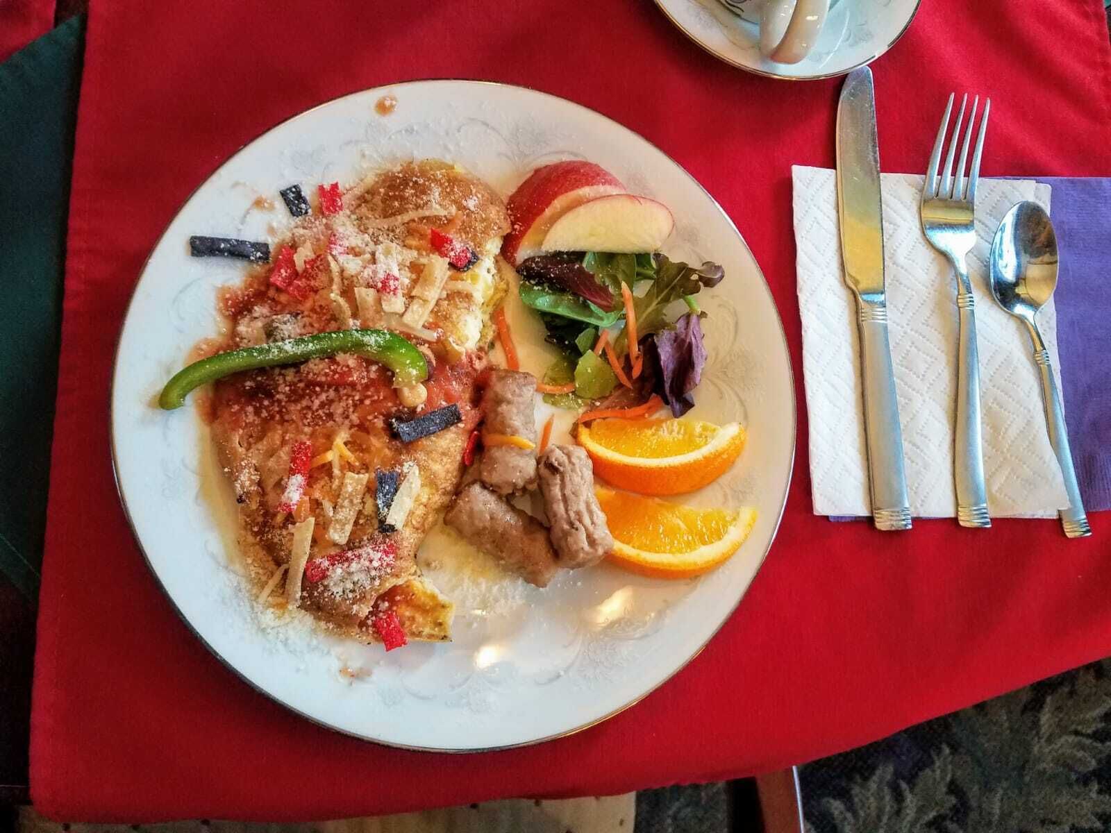 Ein Teller Essen mit Salat und Orangenscheiben auf einer roten Tischdecke.