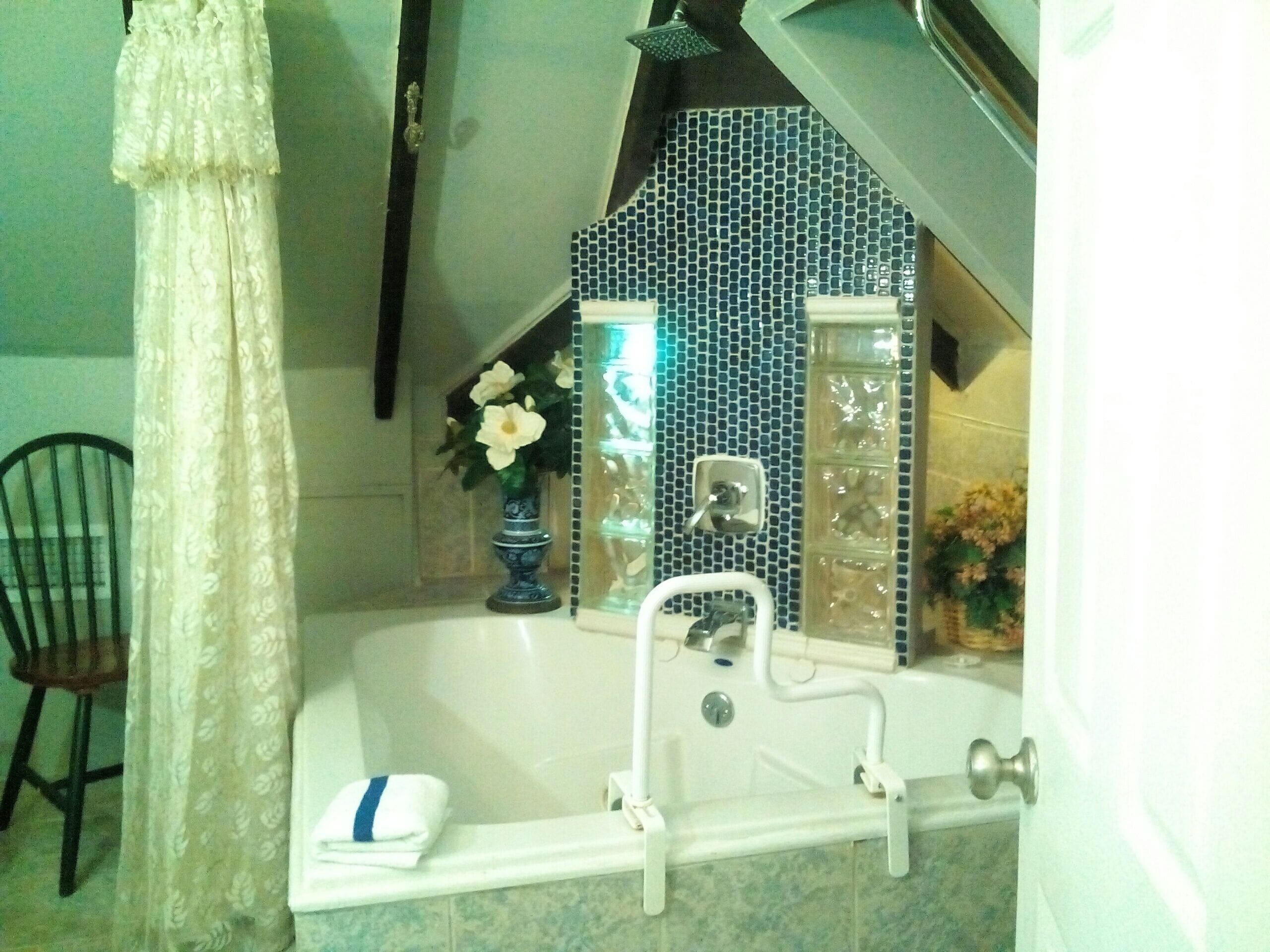 A bathroom with a bathtub, a white sink, and a shower. There is a chair and a vase with flowers on the counter.