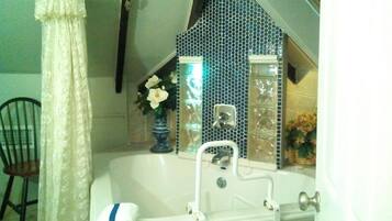 A bathroom with a bathtub, a white sink, and a shower. There is a chair and a vase with flowers on the counter.