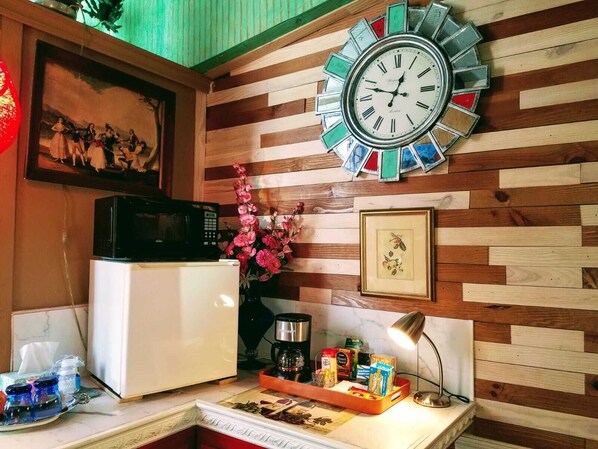 Una cocina con pared de madera, un reloj, un microondas, un refrigerador, una cafetera y varios utensilios de cocina sobre la encimera.