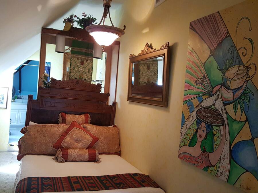 A bedroom with a bed, a painting, a mirror, and a staircase leading to an upper floor.