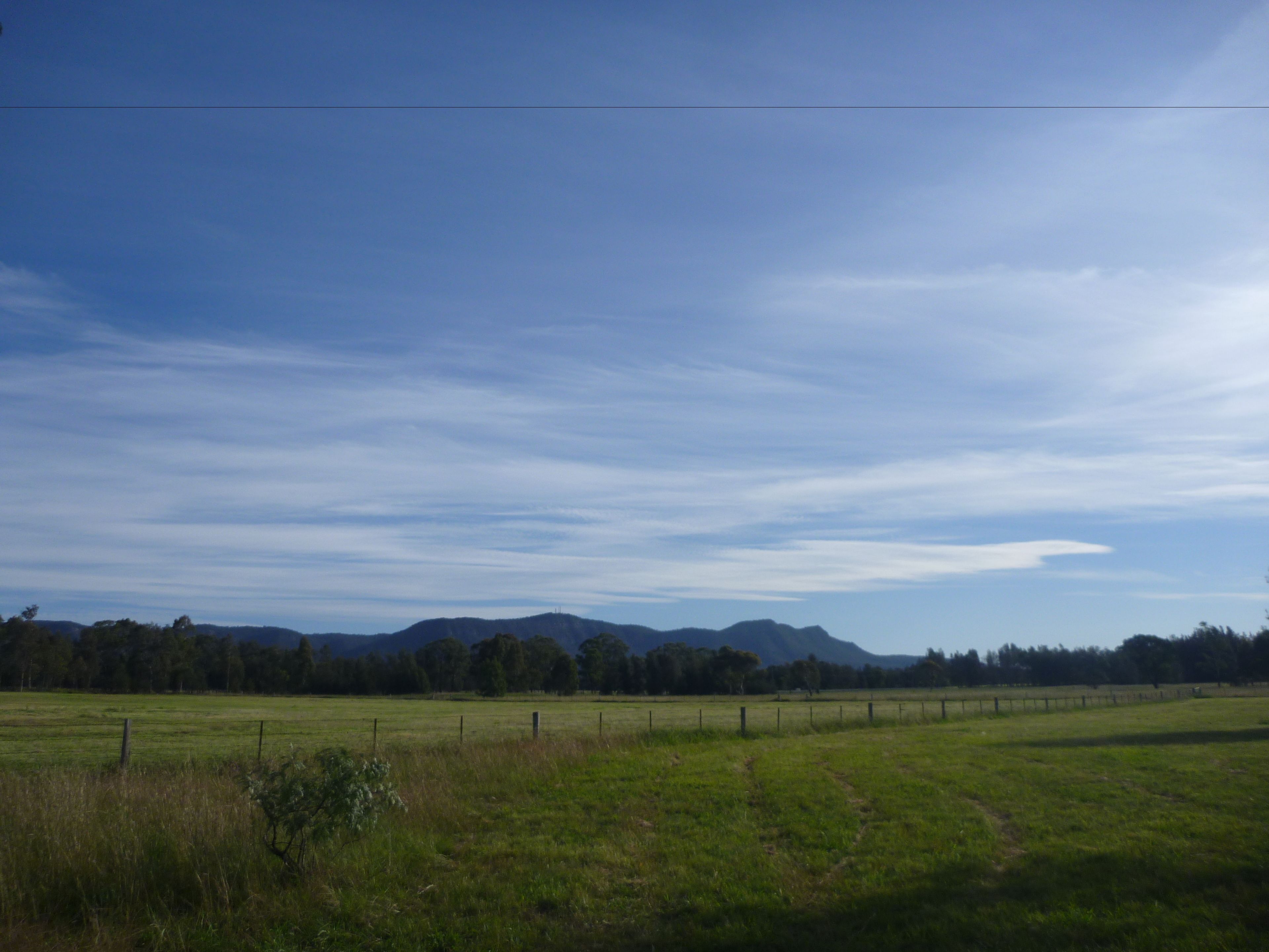 A rural landscape with a clear sky, a fenced field, and distant mountains.