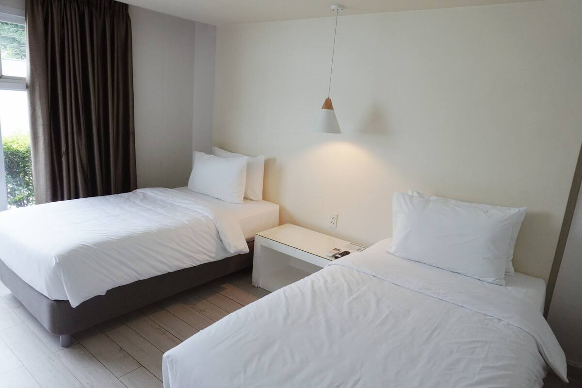 Et hotelværelse med to senge, et natbord, en lampe og et vindue med gardiner.