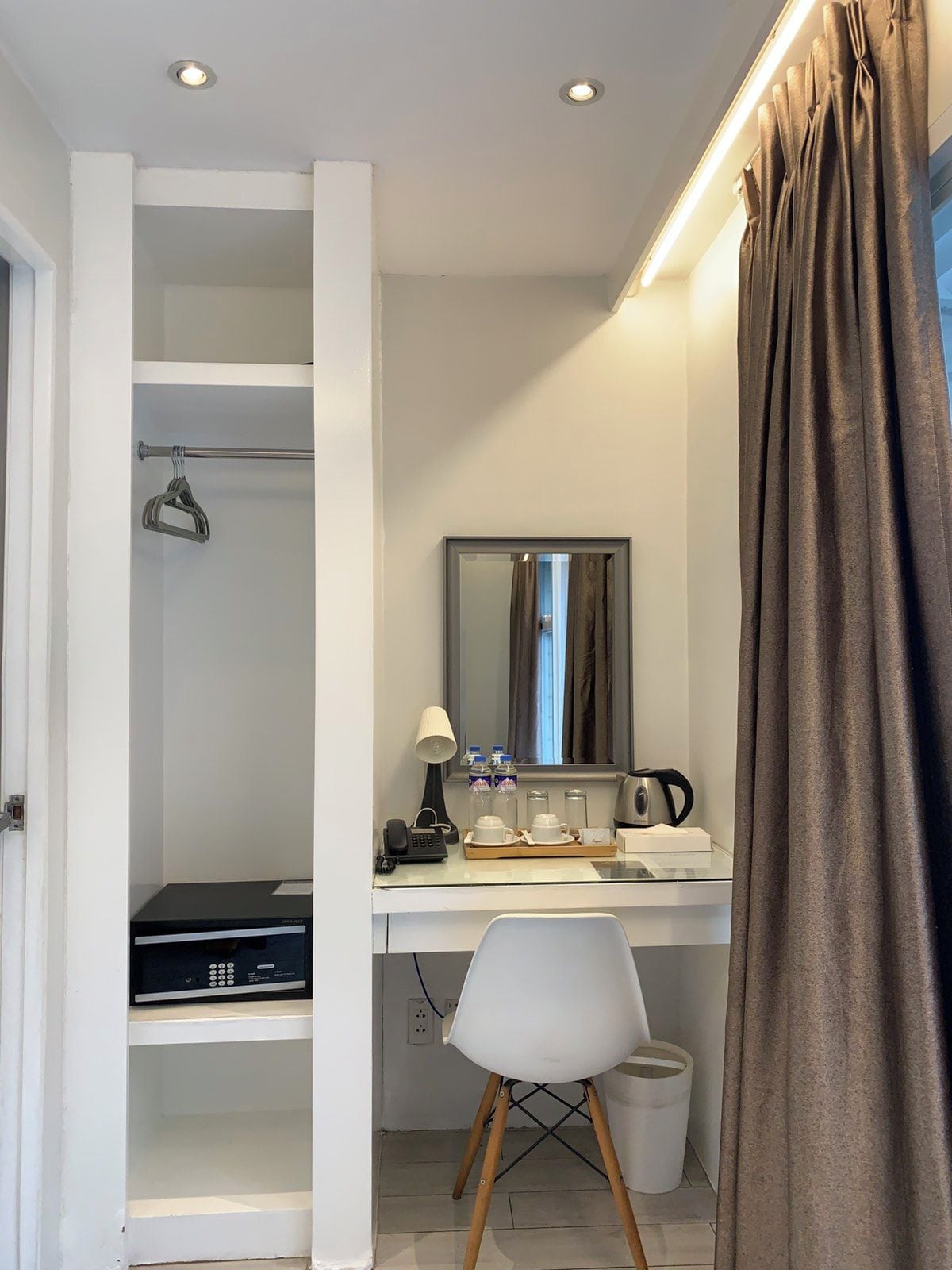 Habitación de hotel con escritorio, silla, espejo, teléfono, tetera y un pequeño cubo de basura.