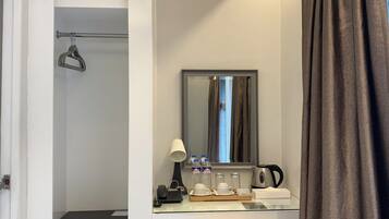 Habitación de hotel con escritorio, silla, espejo, teléfono, tetera y un pequeño cubo de basura.