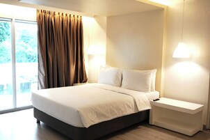 Una habitación de hotel moderna con una cama grande, una mesita de noche y una ventana con cortinas.