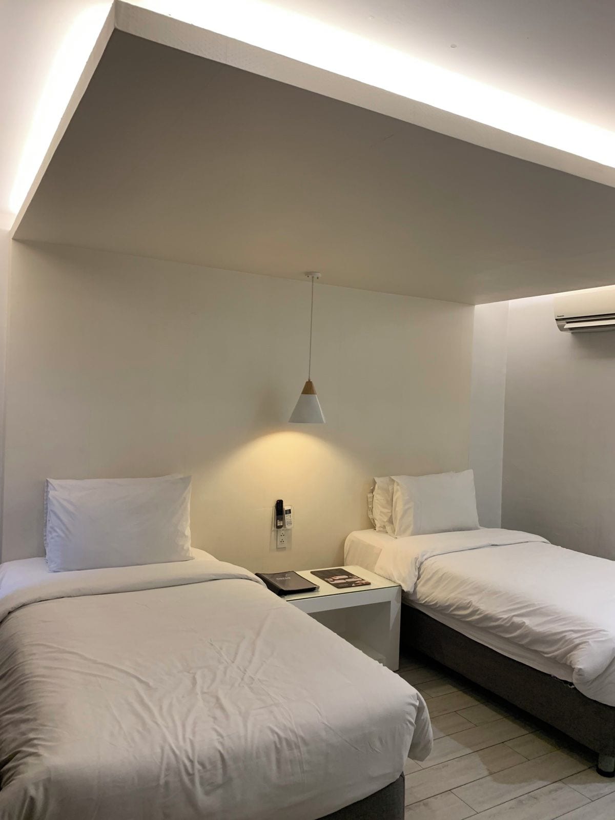 Una habitación de hotel con dos camas, una mesita de noche con lámpara y un equipo de aire acondicionado en la pared.