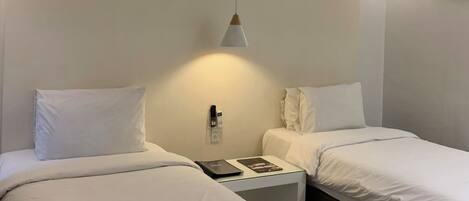 Una habitación de hotel con dos camas, una mesita de noche con lámpara y un equipo de aire acondicionado en la pared.