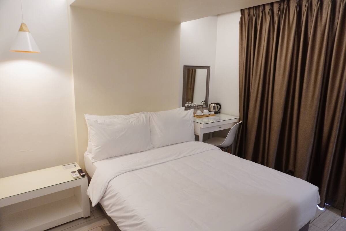 Et hotelværelse med seng, natbord, skrivebord, stol og et spejl.