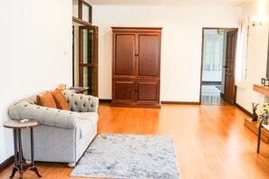 A living room with a grey sofa, a small round table, a large wooden cabinet, and a grey rug. - A Taste of Europe in Chiang Mai (Chiang Mai)