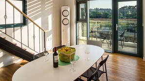 A modern dining area with a white table, black chairs, a wine bottle, and a bowl of fruit. - Poema Stay (Jeju City)