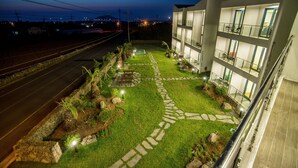 A well-maintained courtyard with a stone pathway, lush green lawn, and a multi-story building with balconies. - Poema Stay (Jeju City)