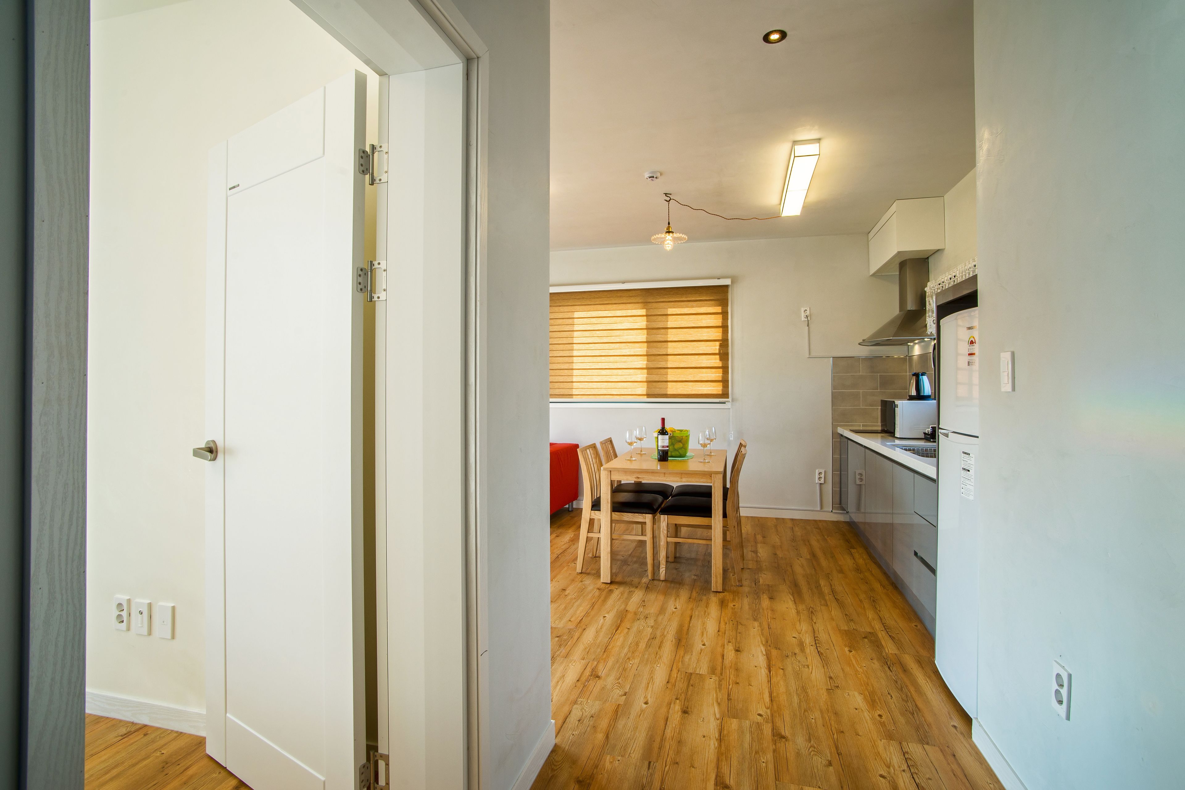 A modern kitchen with wooden flooring, a dining area with a table and chairs, and a red sofa in the background.