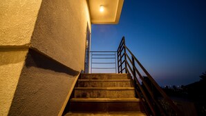 A staircase leading up to a door with a metal railing, a ceiling light, and a clear sky in the background. - Poema Stay (Jeju City)