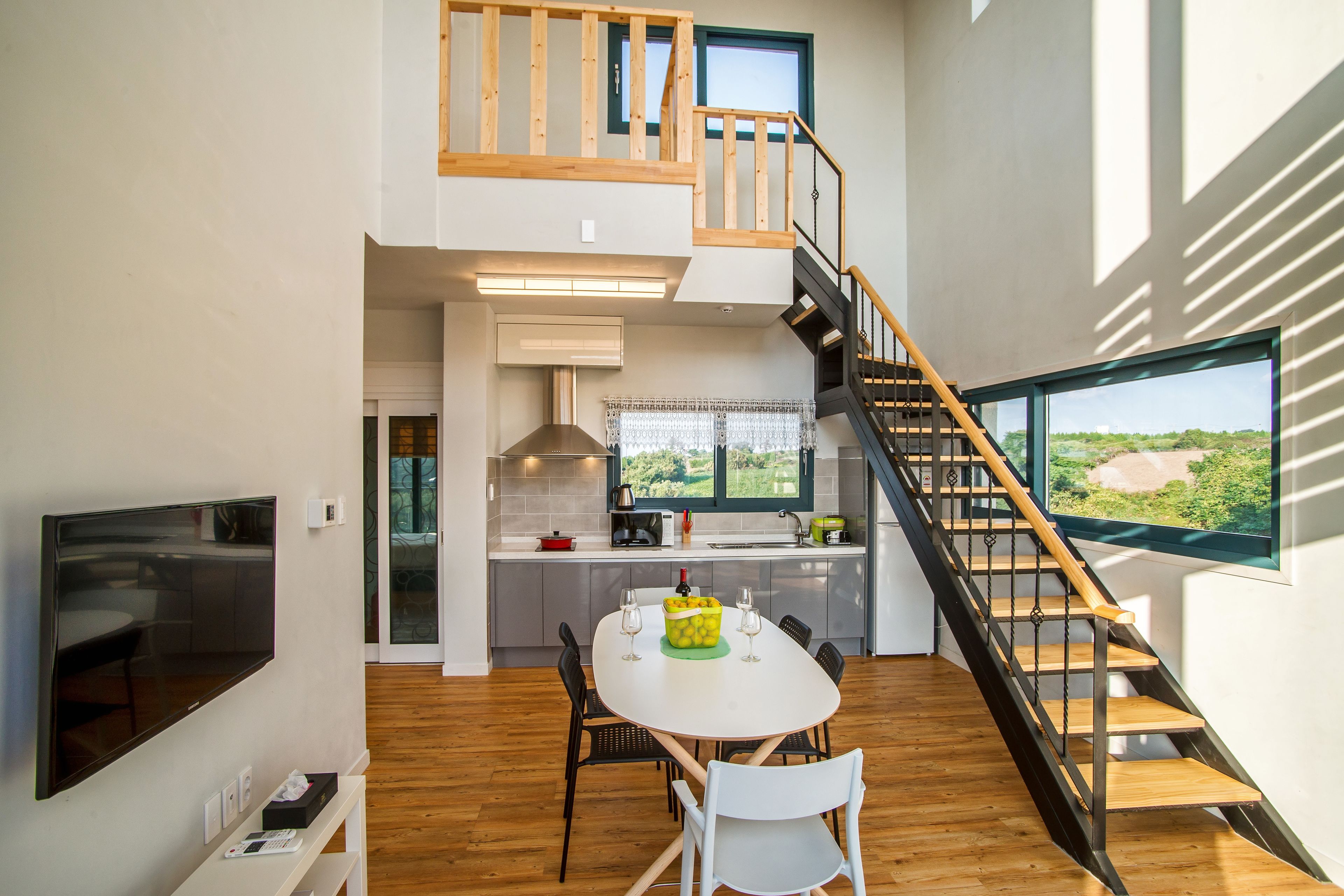 A modern kitchen with a dining area, a staircase, and large windows. - Poema Stay (Jeju City)