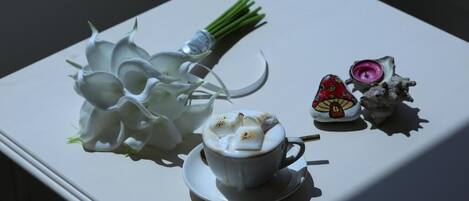A white table with a cup of coffee, a bouquet of white flowers, and a decorative item.