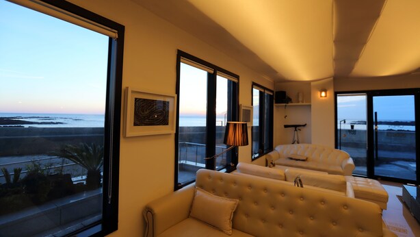 Una sala de estar moderna con un ventanal grande que da a una playa, un sofá y una lámpara.