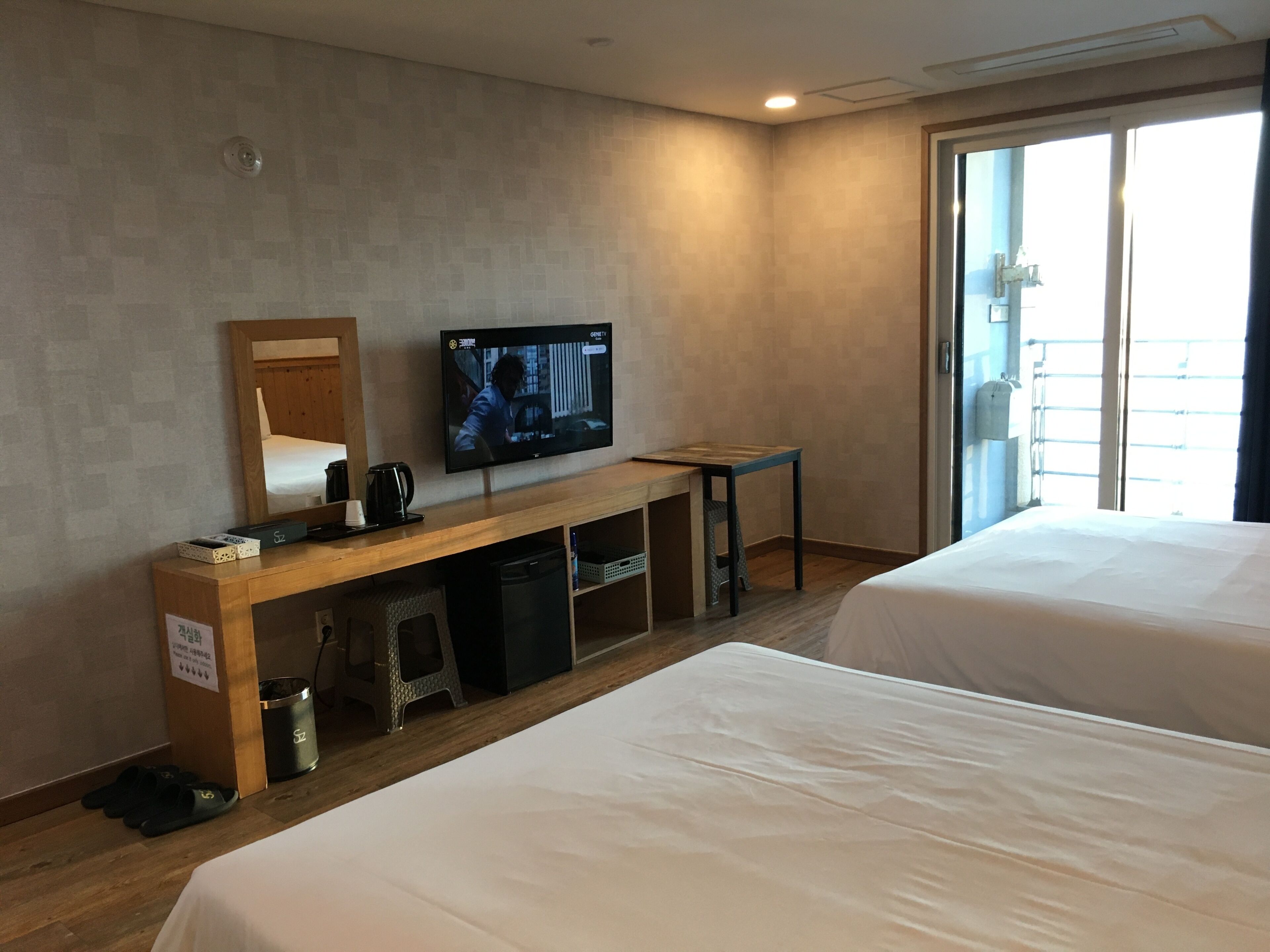 Une chambre d’hôtel avec deux lits, un téléviseur fixé au mur, un bureau en bois, une poubelle et une fenêtre donnant sur un beau paysage.