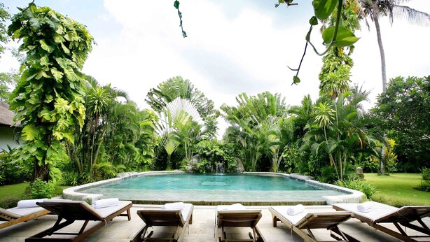 A poolside area with lounge chairs and a clear view of a waterfall. - Bali Hidden Paradise Villa (Seminyak)