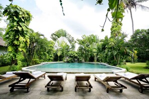 A poolside area with lounge chairs and a clear view of a waterfall. - Bali Hidden Paradise Villa (Seminyak)
