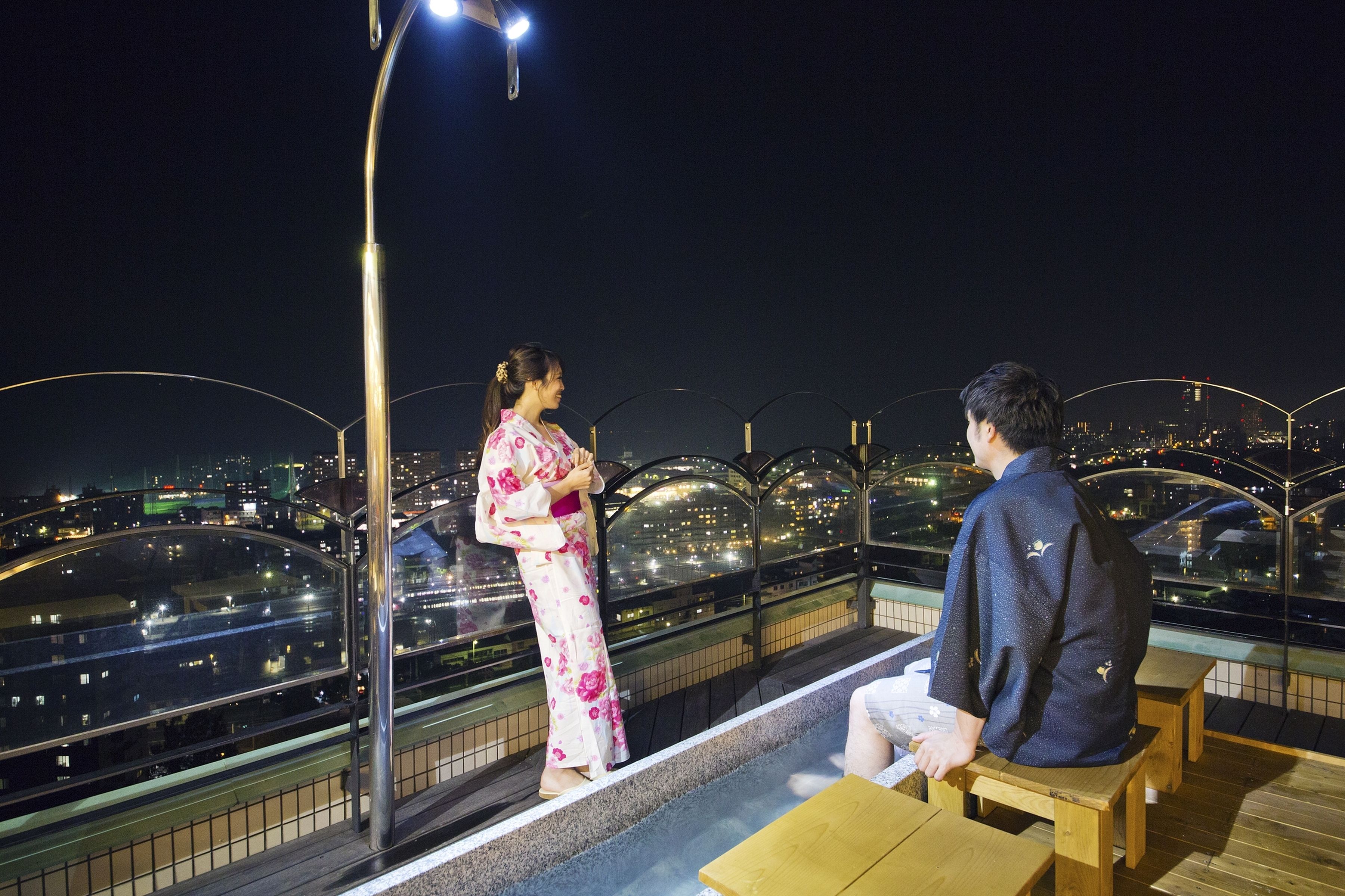 A couple sitting on a wooden bench overlooking a cityscape at night.