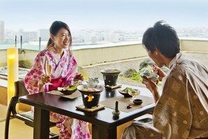 Une table à manger dressée avec des plats traditionnels japonais, un réchaud portable et une vue sur la ville en arrière-plan.