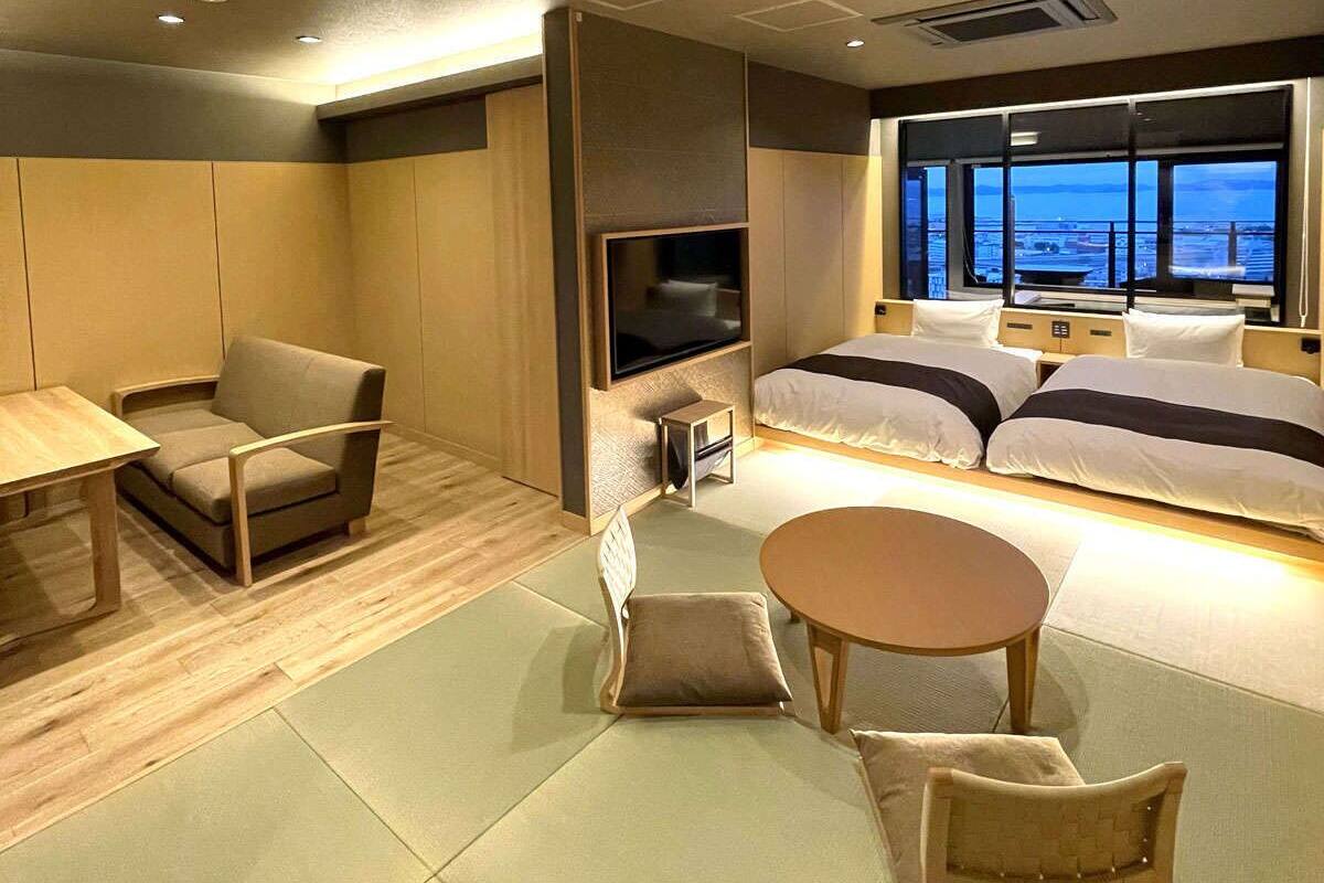 Habitación de hotel moderna con sofá, una mesita, televisor y cama con vista a la ciudad.