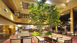 Un hall espacioso con asientos escalonados, un árbol central y una mesa de recepción.