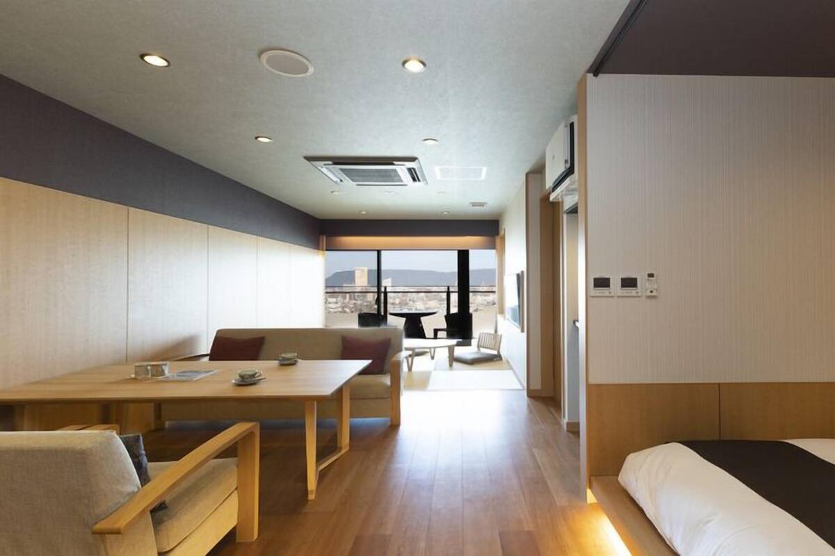 Habitación de hotel moderna con suelo de madera, cama, escritorio y balcón con vistas a la ciudad.