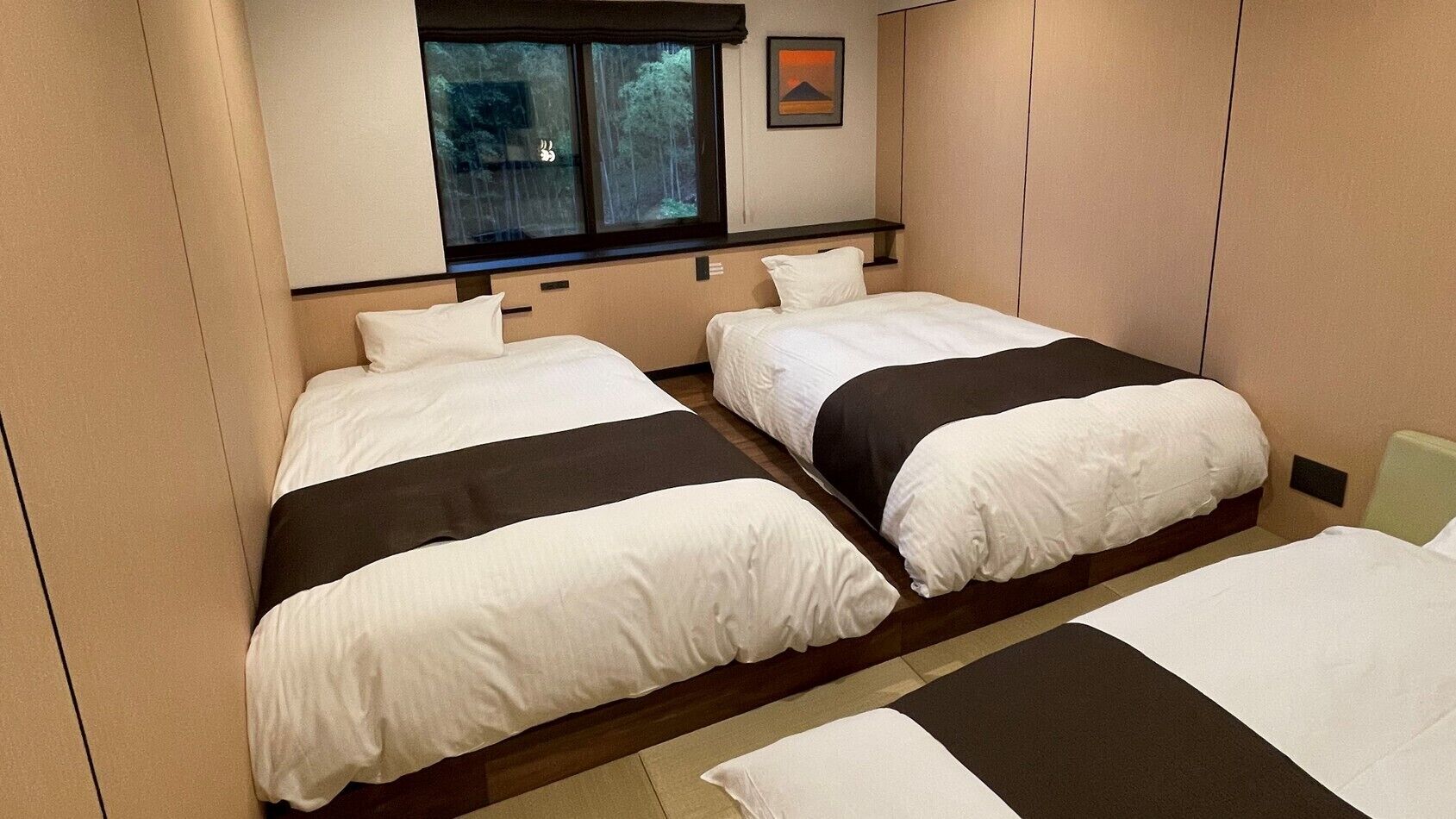 A hotel room with two beds, a window with a view of trees, and a framed picture on the wall.