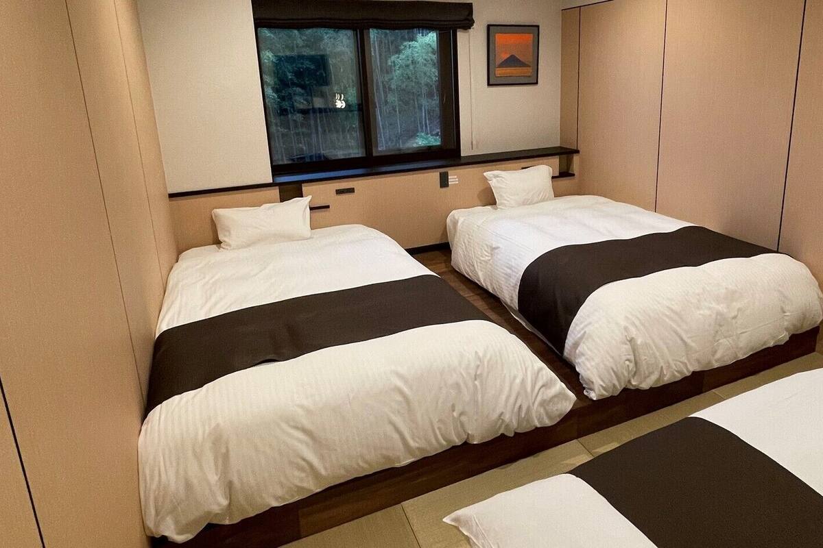 A hotel room with two beds, a window with a view of trees, and a framed picture on the wall.
