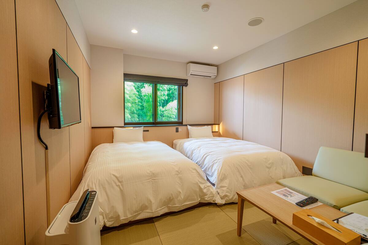 Habitación de hotel con dos camas, un sofá, una mesa, un televisor y una ventana con vista a árboles.
