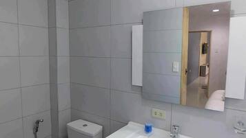 A modern bathroom with grey tiles, a white toilet, a sink with a mirror above it, and a shower area.