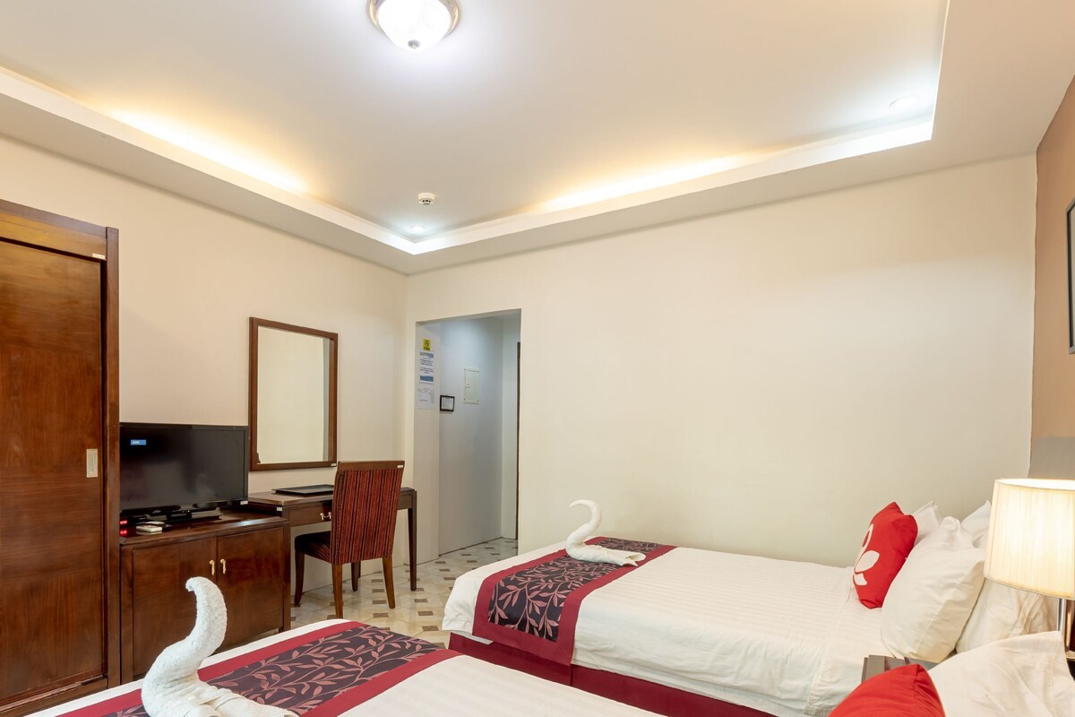 A hotel room with two beds, a desk with a computer, a wardrobe, and a mirror.