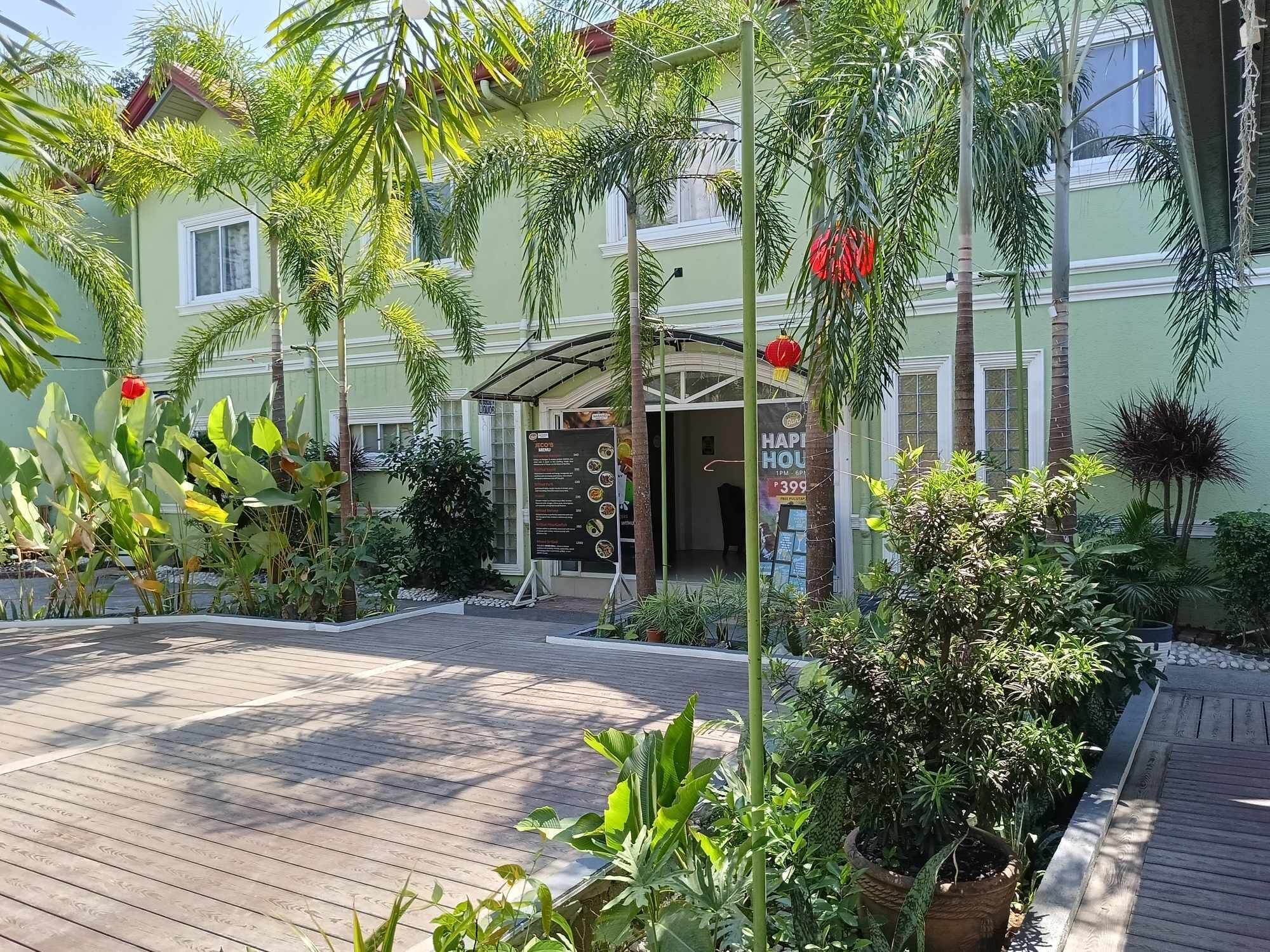 A hotel entrance with a covered patio area, surrounded by lush greenery and potted plants.
