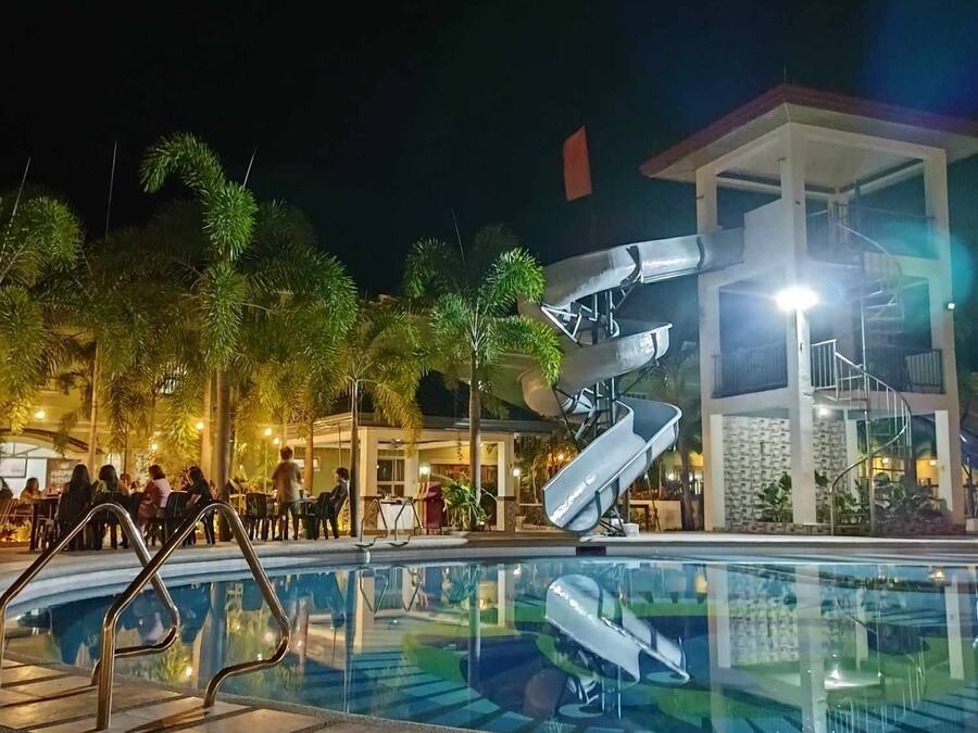 Ein Pool mit moderner Rutsche, umgeben von Palmen und einem Gebäude mit einer Wendeltreppe.