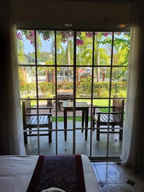 Una habitación con un ventanal grande que da a un patio con mobiliario exterior y vistas a un jardín y edificios.