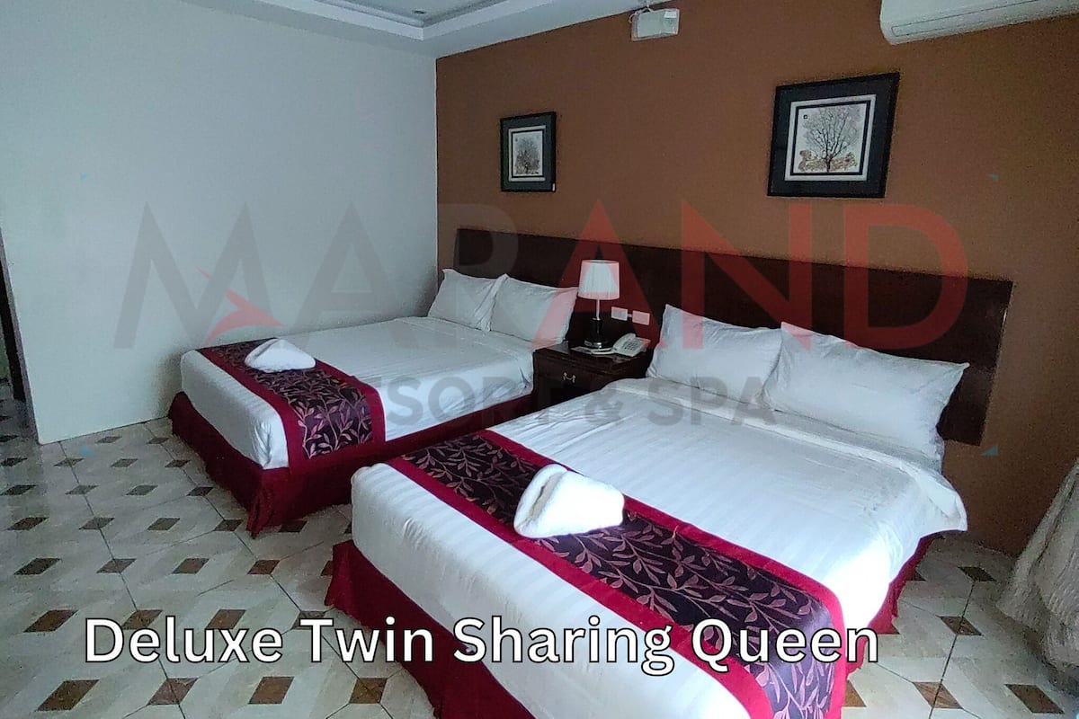A Deluxe Twin Sharing Queen room with two beds, a nightstand, a lamp, and two framed pictures on the wall.