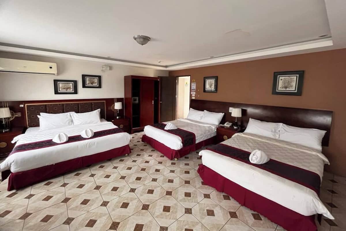 A hotel room with three beds, each with white linens and red accents, arranged in a row.
