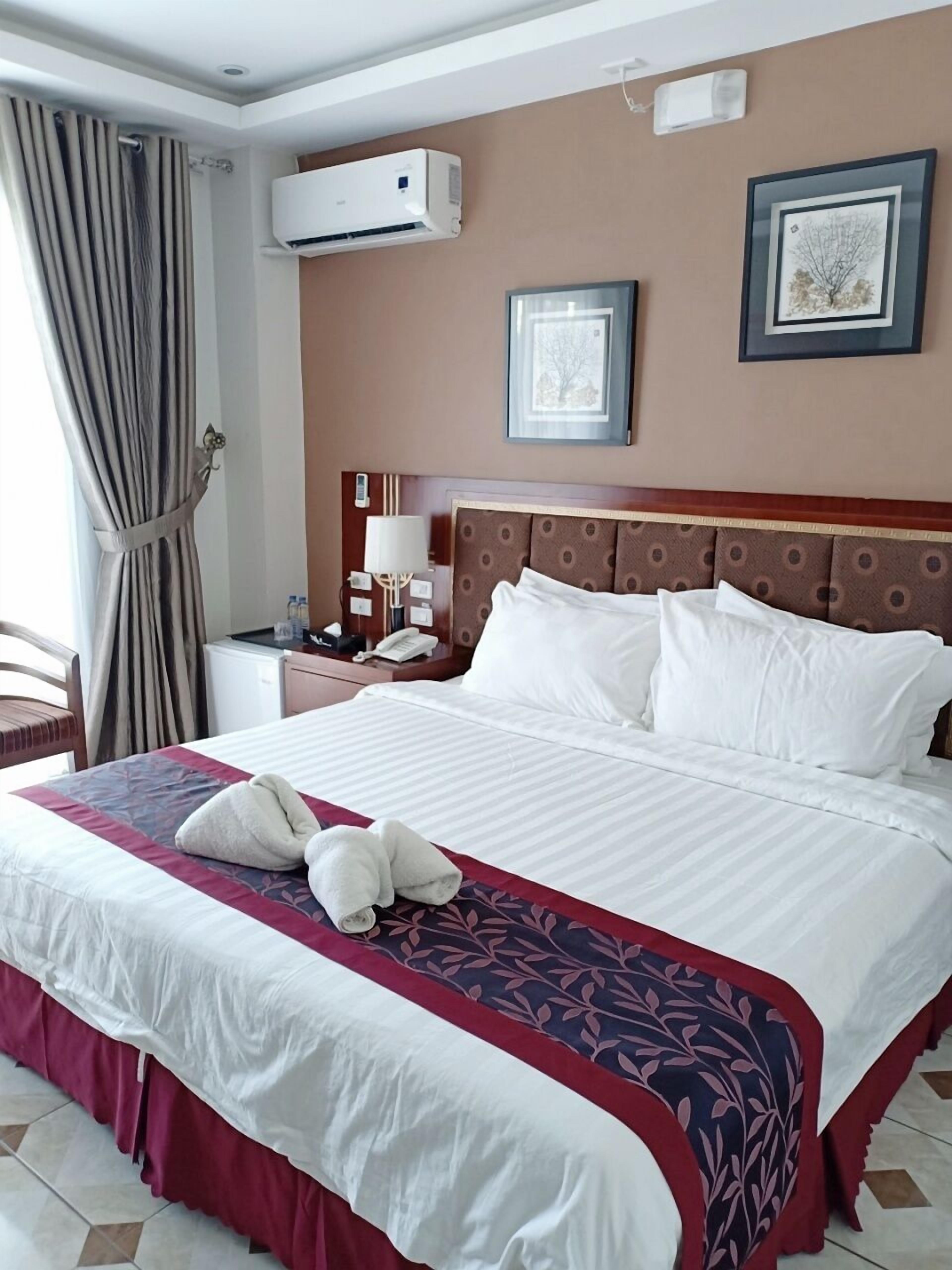 Habitación de hotel con una cama grande, una mesita de noche, un equipo de aire acondicionado y un cuadro en la pared.