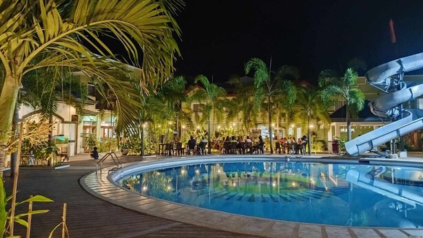A nighttime pool area with a circular pool, palm trees, and people around tables and chairs. - Marand Family Resort (Bauang)