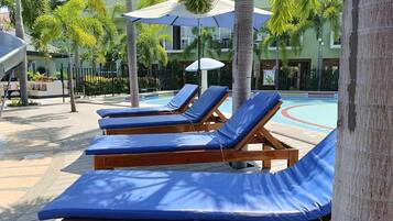 Un espace aménagé au bord de la piscine, avec des chaises longues en bois et des parasols.