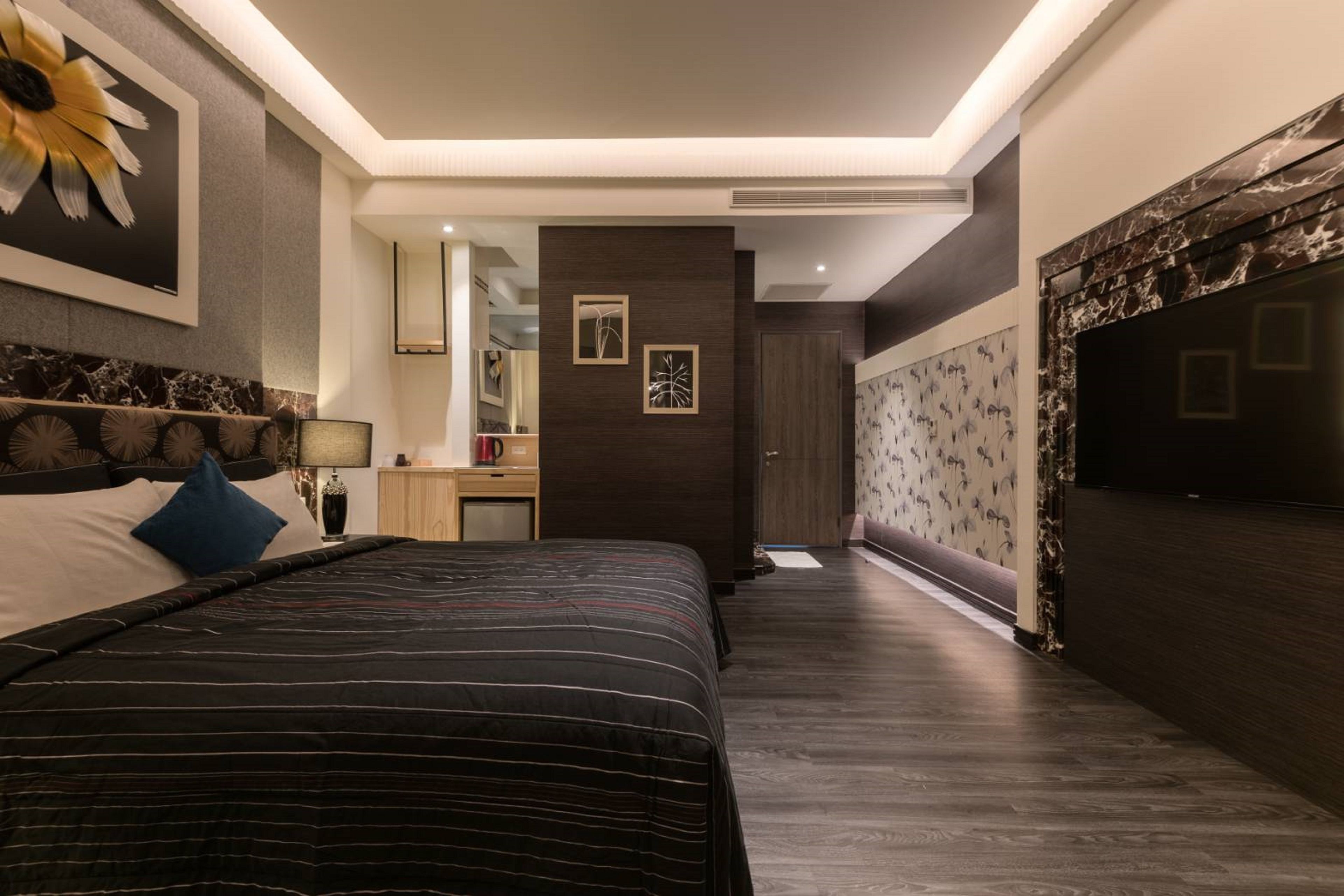 A modern bedroom with a large bed, a nightstand, a mirror, and a dark wooden wall with a floral pattern.