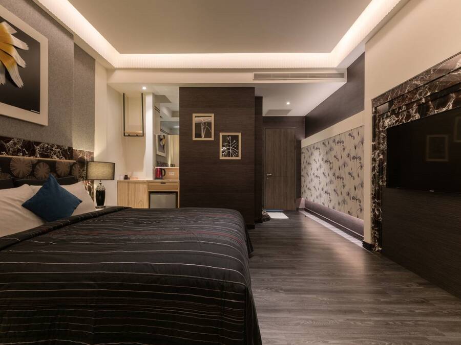 A modern bedroom with a large bed, a nightstand, a mirror, and a dark wooden wall with a floral pattern.